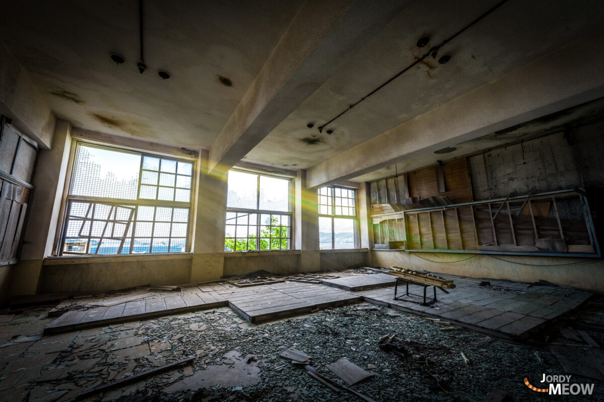 Sunlit abandoned classroom on Gunkanjima, Nagasaki, with crumbling walls and debris.