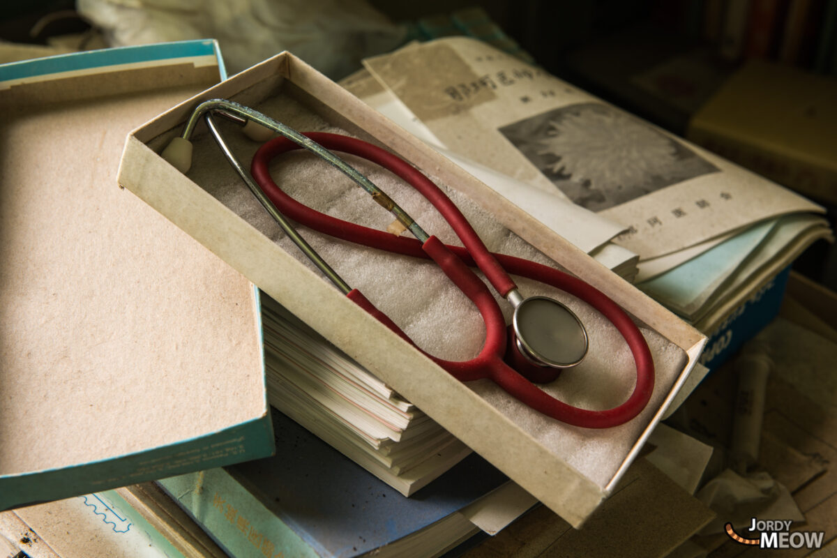 Red stethoscope in box atop yellowed files inside abandoned White Clinic hospital ruin