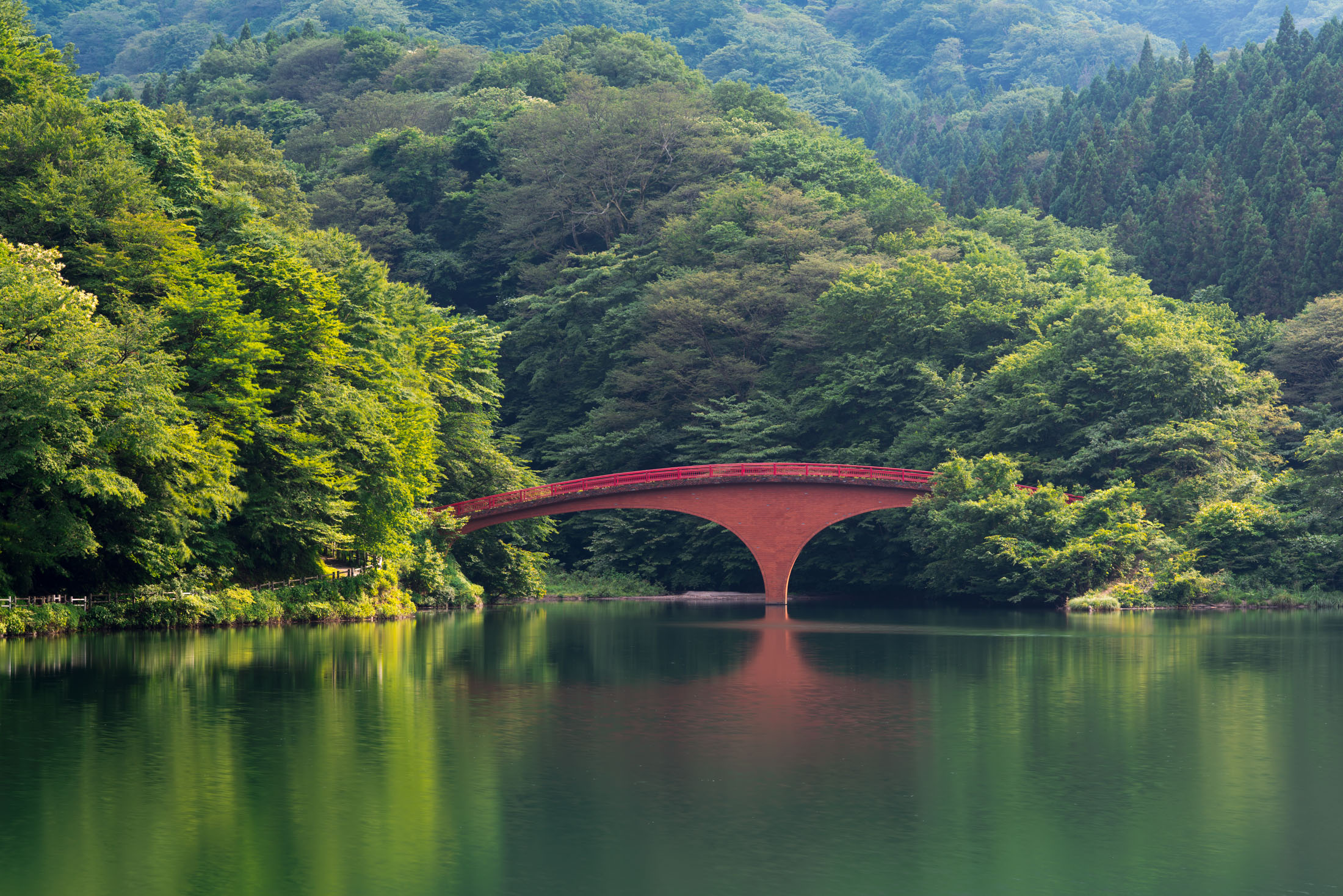 Red arch bridge reflecting on calm forest lake in Gunma, Japan