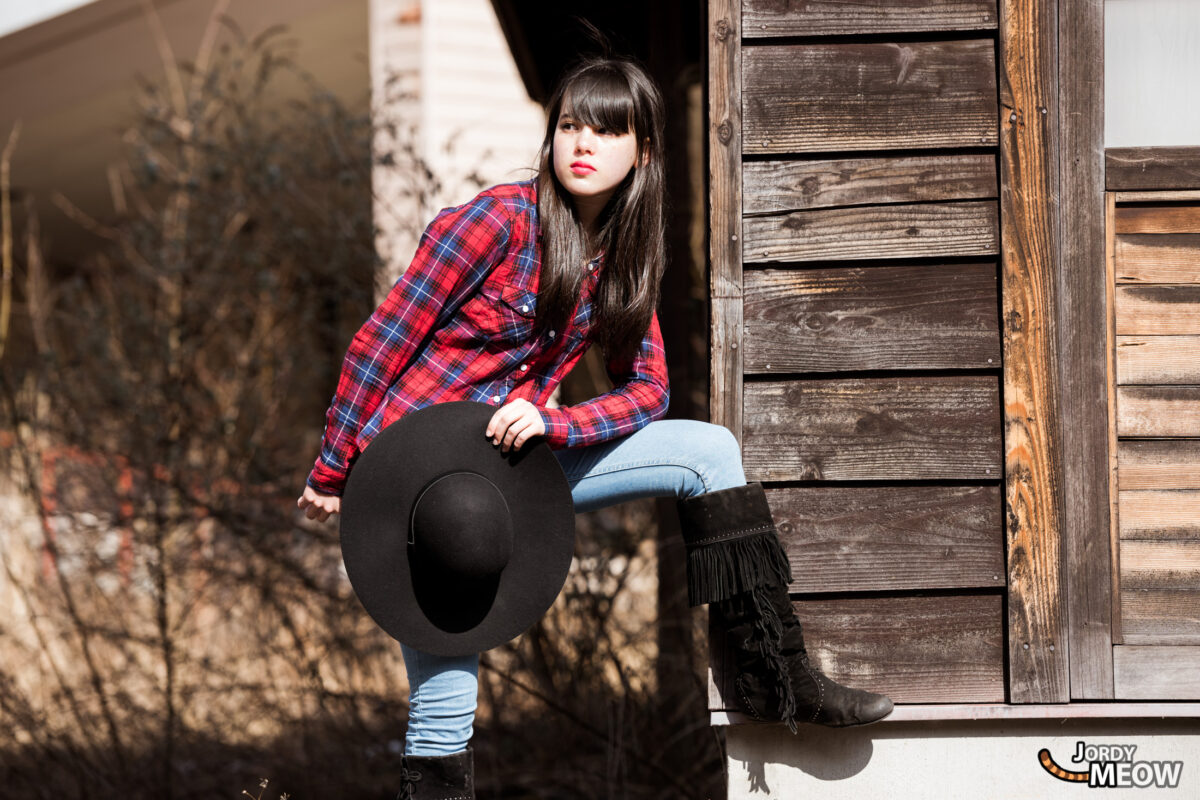 Woman holding cowboy hat in Japan’s abandoned Western Village theme park, weathered wooden buildings