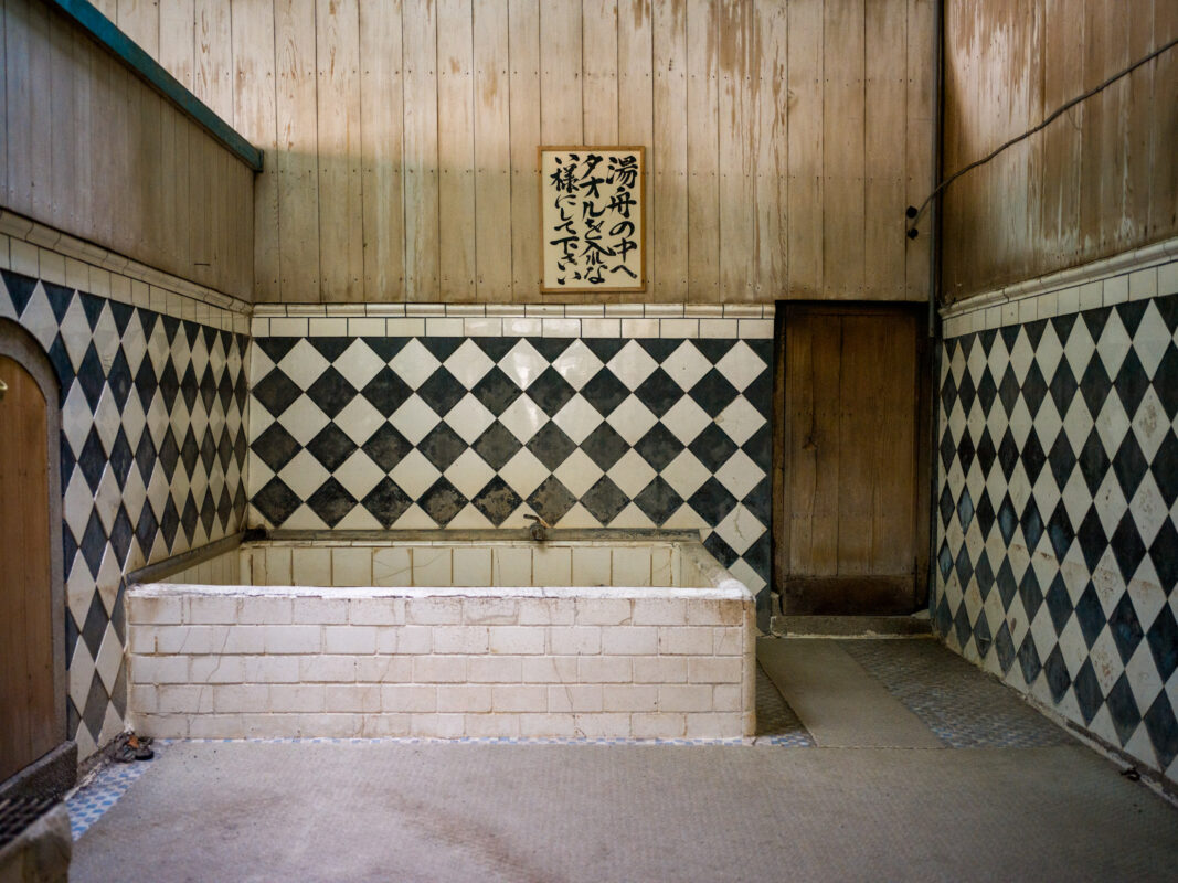 Empty vintage Japanese bathhouse interior with tiled soaking tub, diamond tiles, and calligraphy sign