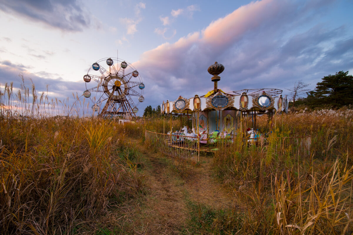 Overgrown abandoned amusement park at dawn with rusted Ferris wheel and faded carousel