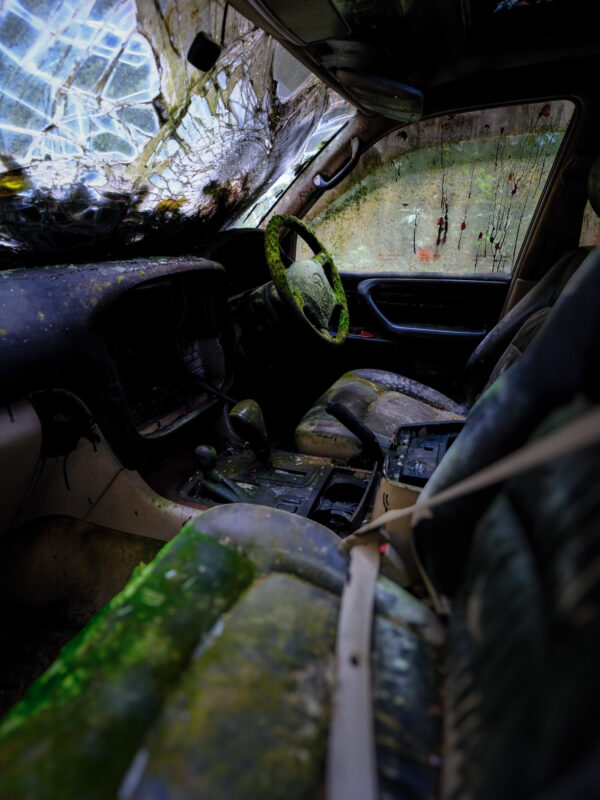 Abandoned Toyota Land Cruiser interior with moss-covered steering wheel and shattered windshield