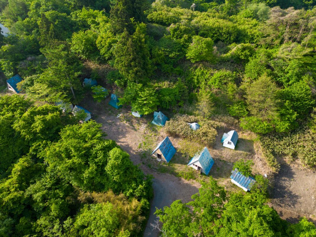 Aerial view of Kejonuma Leisure Land forest cabins with blue roofs and winding paths.