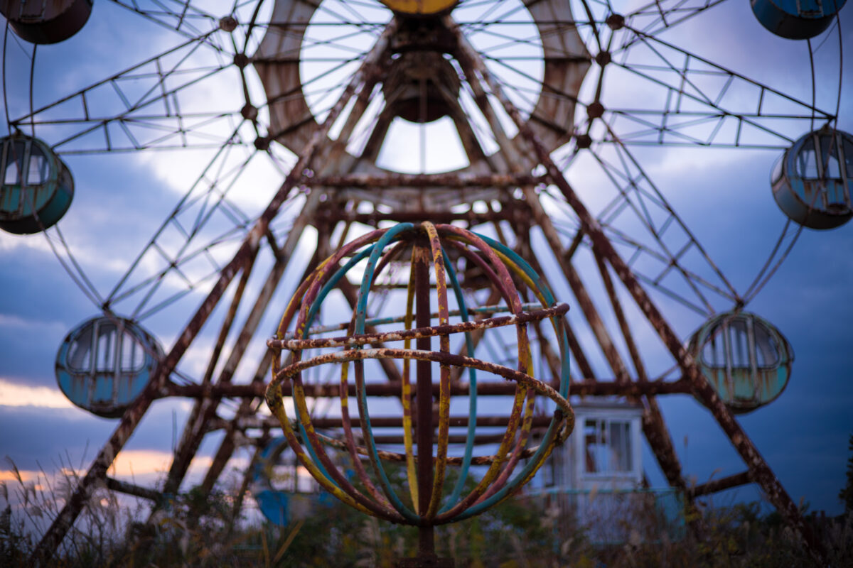 Rusted sphere and Ferris wheel at abandoned Kejonuma Leisure Land amusement park under gray sky