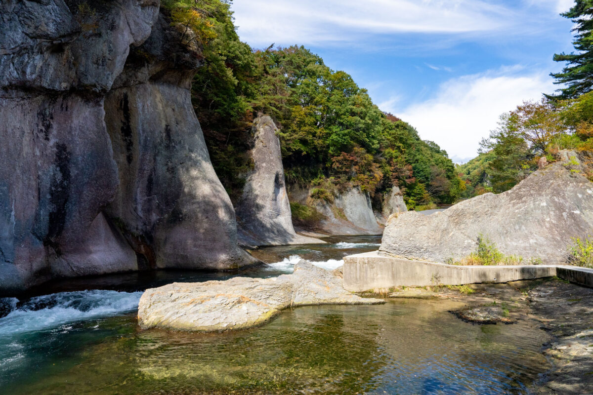 Fukiware Falls gorge with rushing river between tall rock cliffs and autumn trees