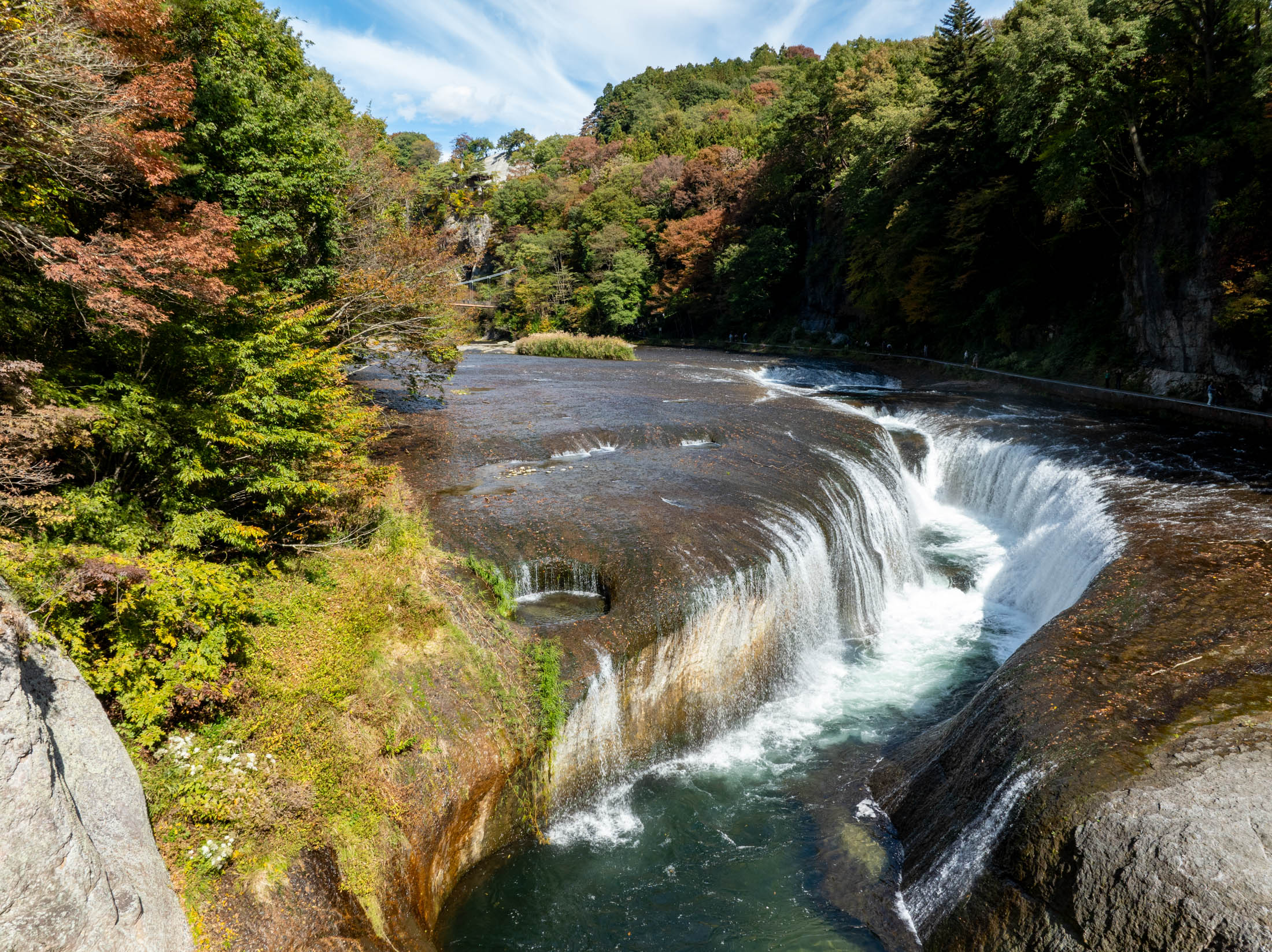 Fukiware Falls in Japan, river rushing through curved rock gorge amid autumn forest.