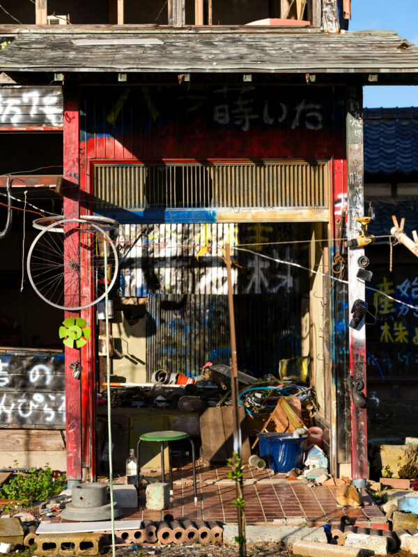 Abandoned shack with graffiti, cluttered interior, and rusted bicycle wheel in daylight