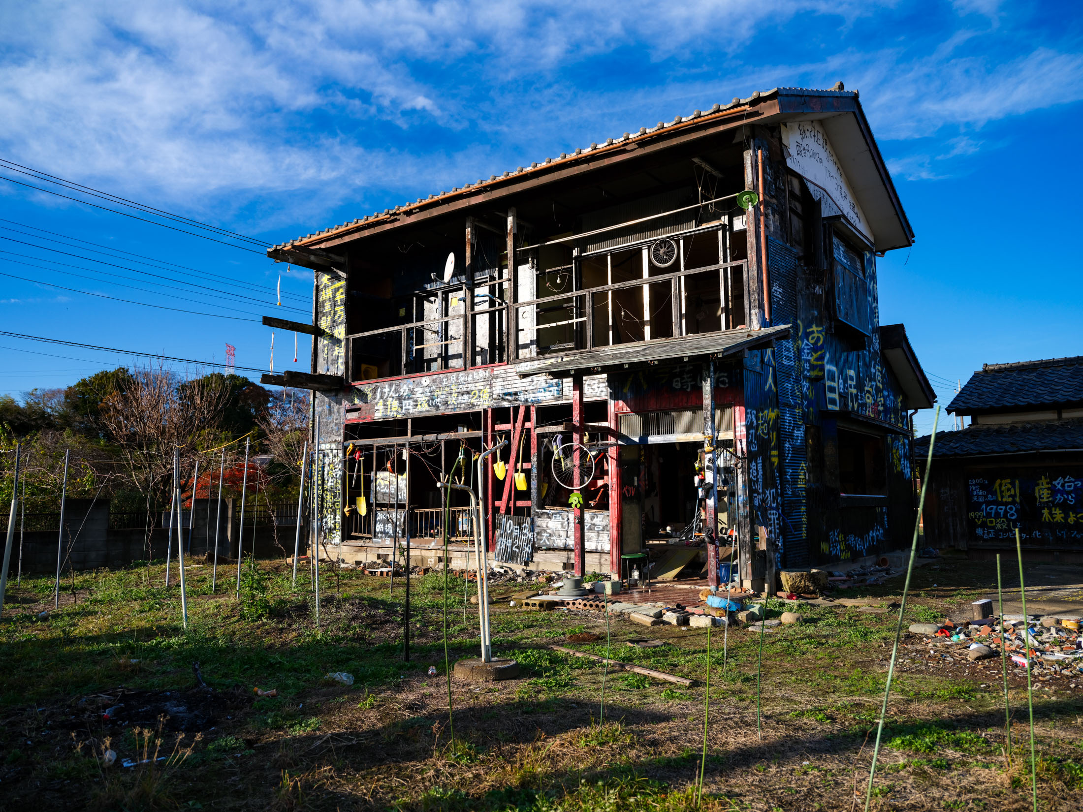 Abandoned black two-story house covered in graffiti beneath a bright blue sky