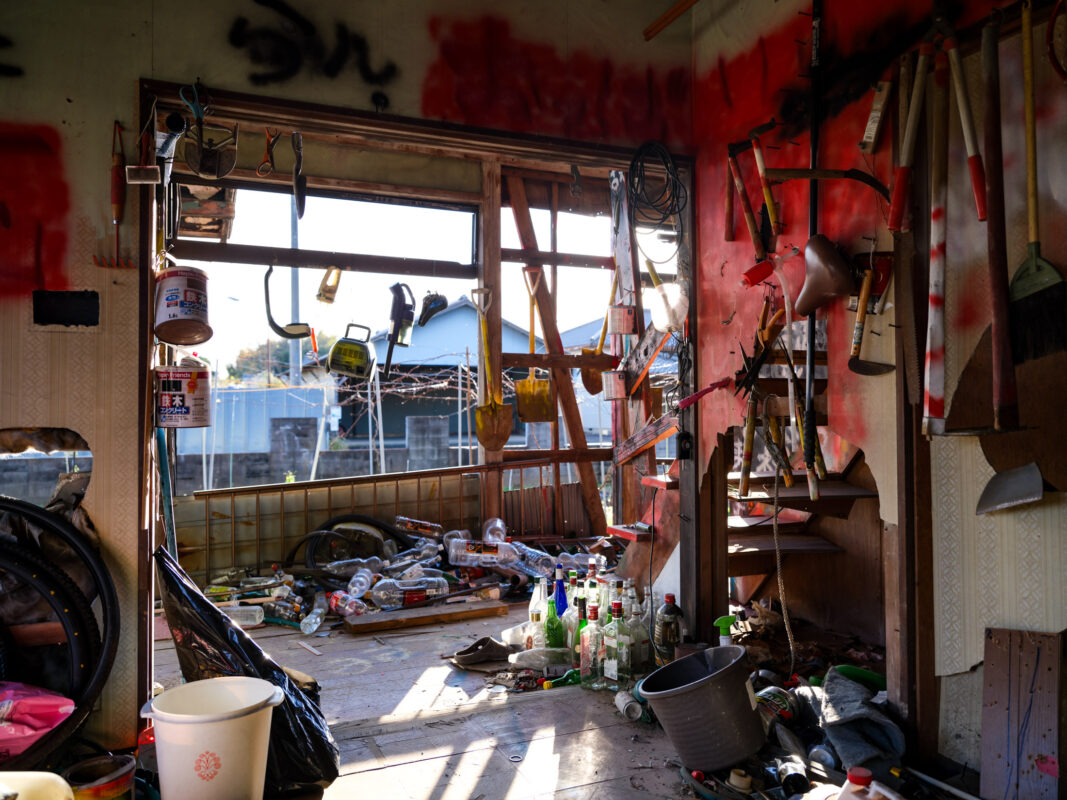 Abandoned house interior with broken window, graffiti splatter, and debris-strewn floor