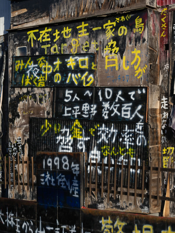 Weathered black wooden house facade with Japanese graffiti and “1998” painted in yellow