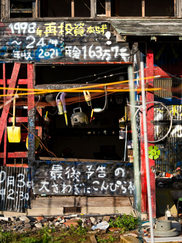 Weathered Japanese black wooden house with graffiti, dates, exposed pipes, and red ladder.