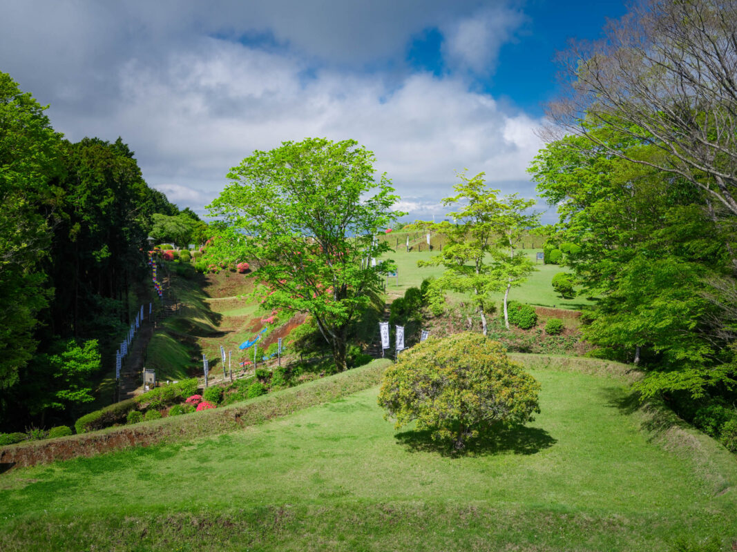 Grassy earthworks and terraced embankments at Yamanaka Castle Ruins, Japan under a partly cloudy sky.
