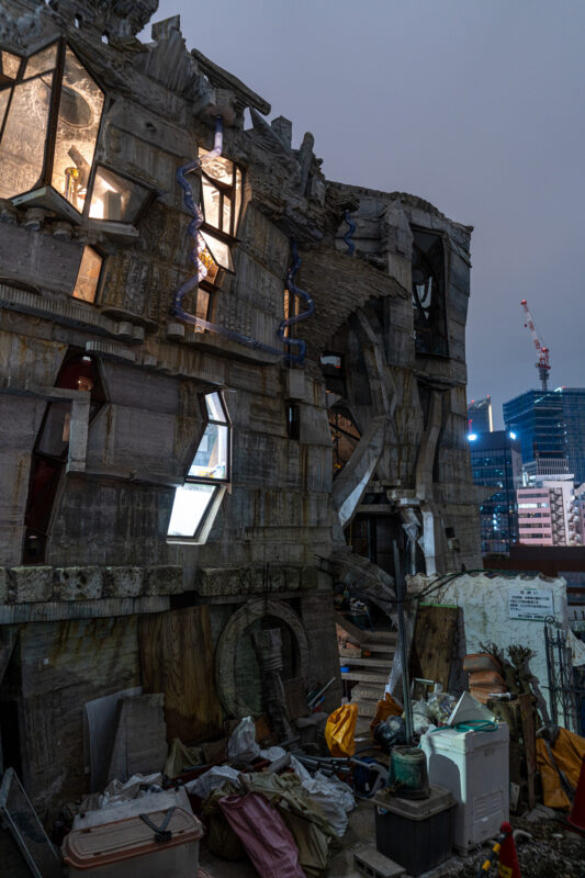 Dilapidated concrete high-rise at dusk with debris and a few lit windows, city backdrop.