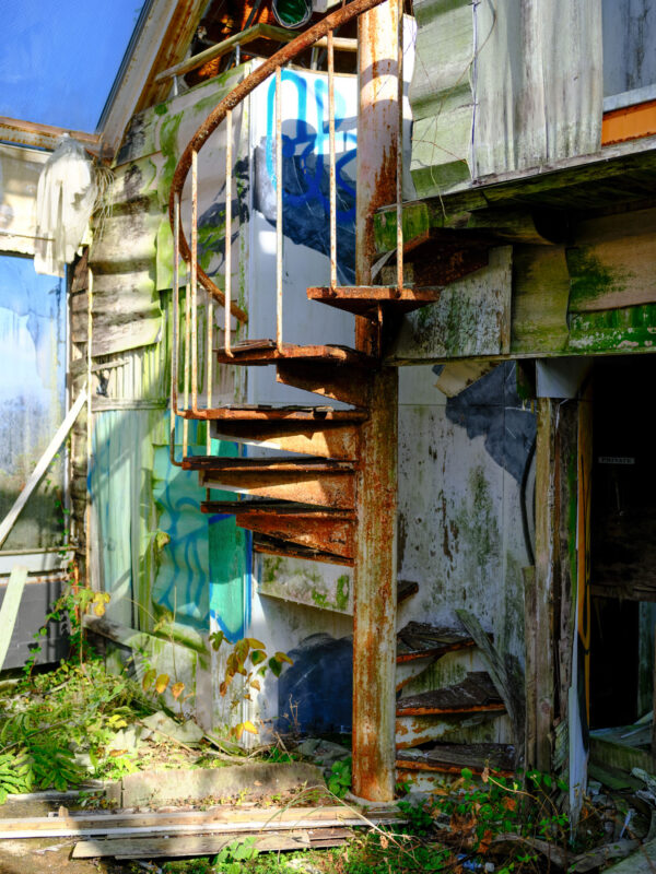 Rusted spiral staircase on abandoned church with peeling paint and dark doorway