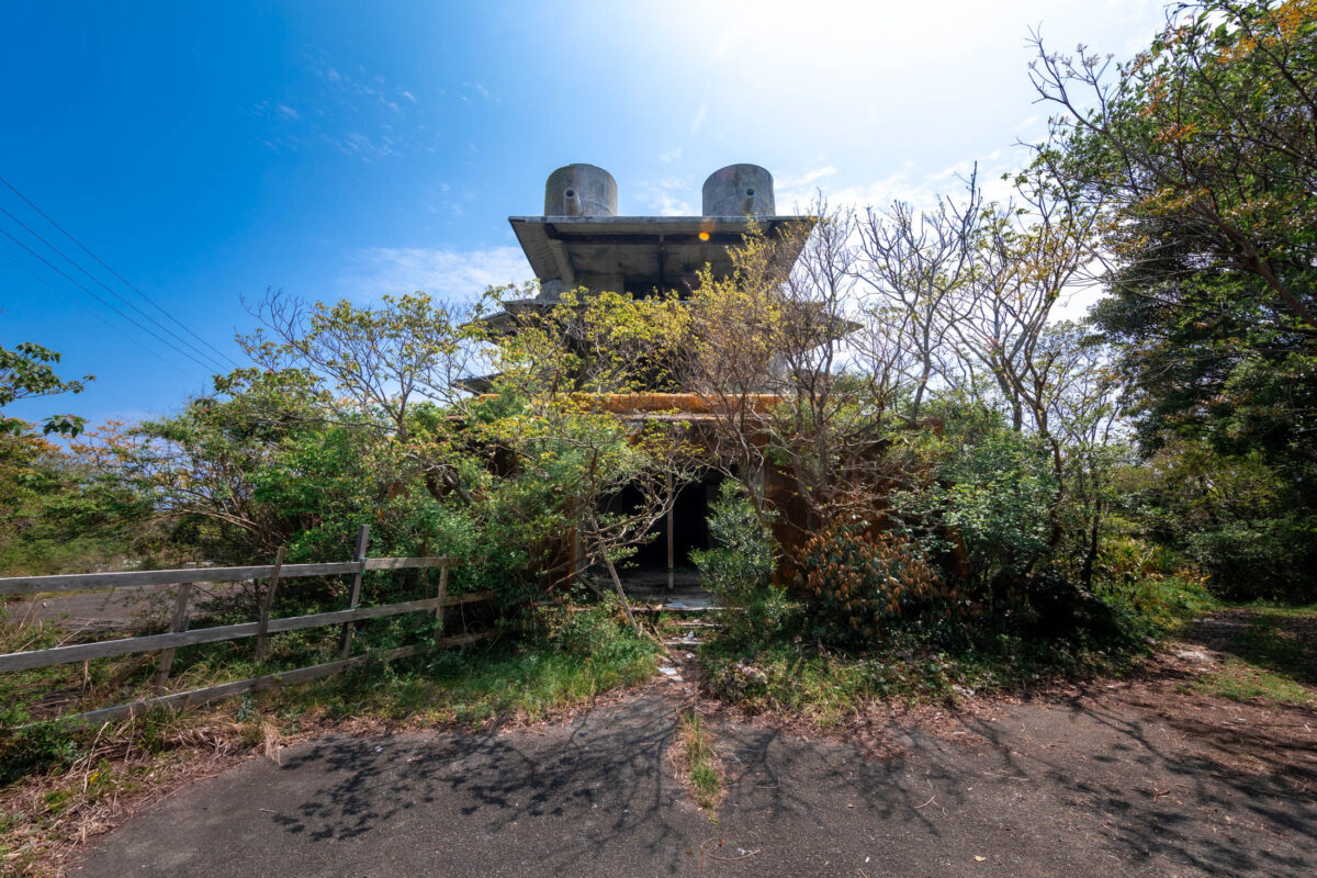 Abandoned brutalist concrete resort with twin towers, overgrown path, clear blue sky