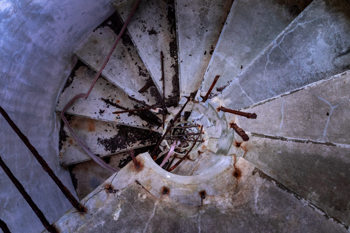Top-down photo of abandoned spiral staircase at Muroto Sky Resort, cracked concrete and rust.
