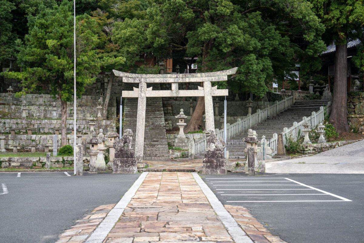 Stone torii gate and shrine steps in Izuhara, Japan, leading into lush forest.