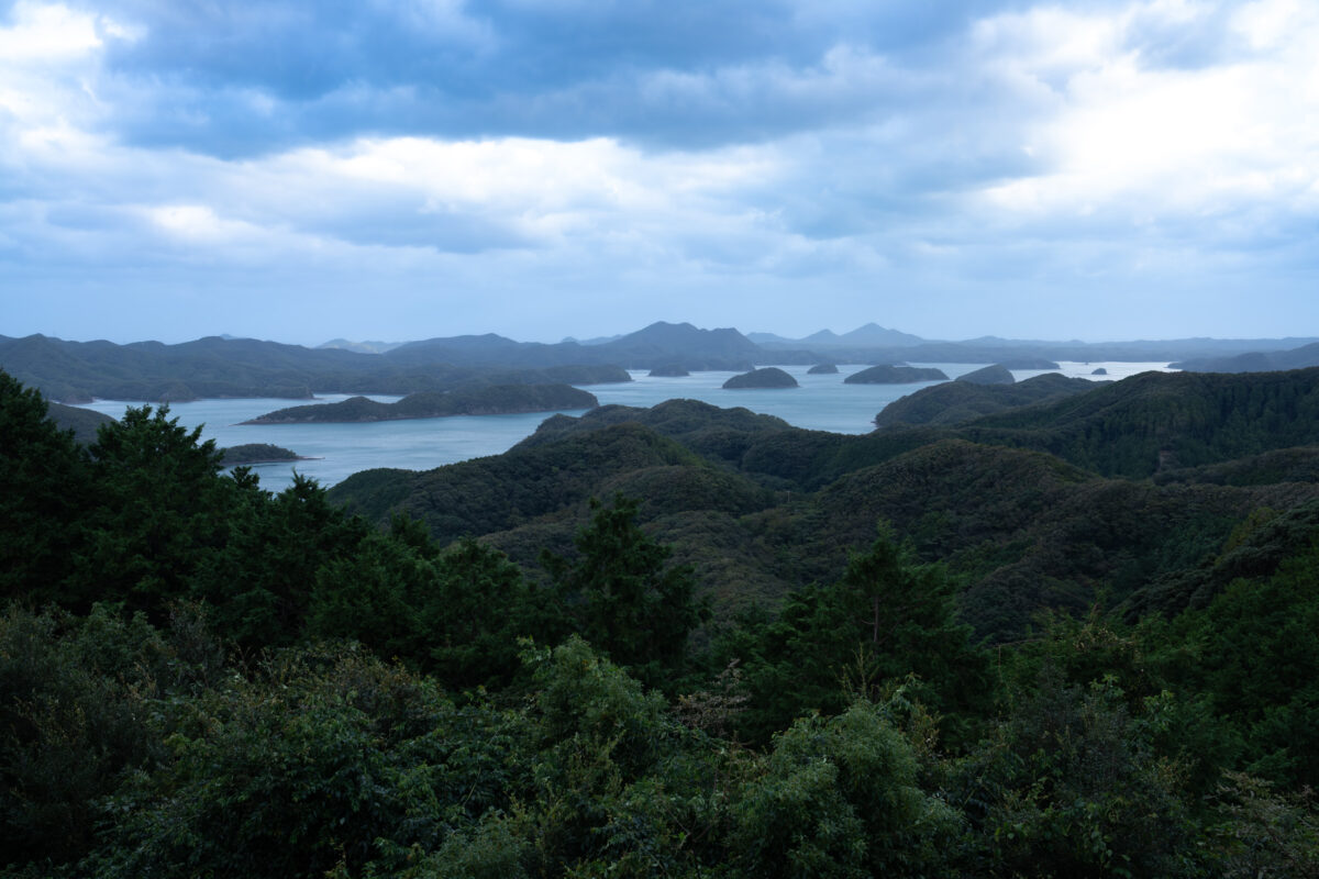 Panoramic view from Mount Eboshi of forested ridges and coastal inlets under overcast sky