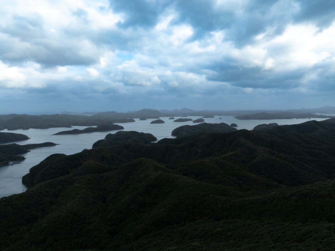 Panoramic Mount Eboshi overlook with forested ridges and island-dotted waters under stormy clouds.