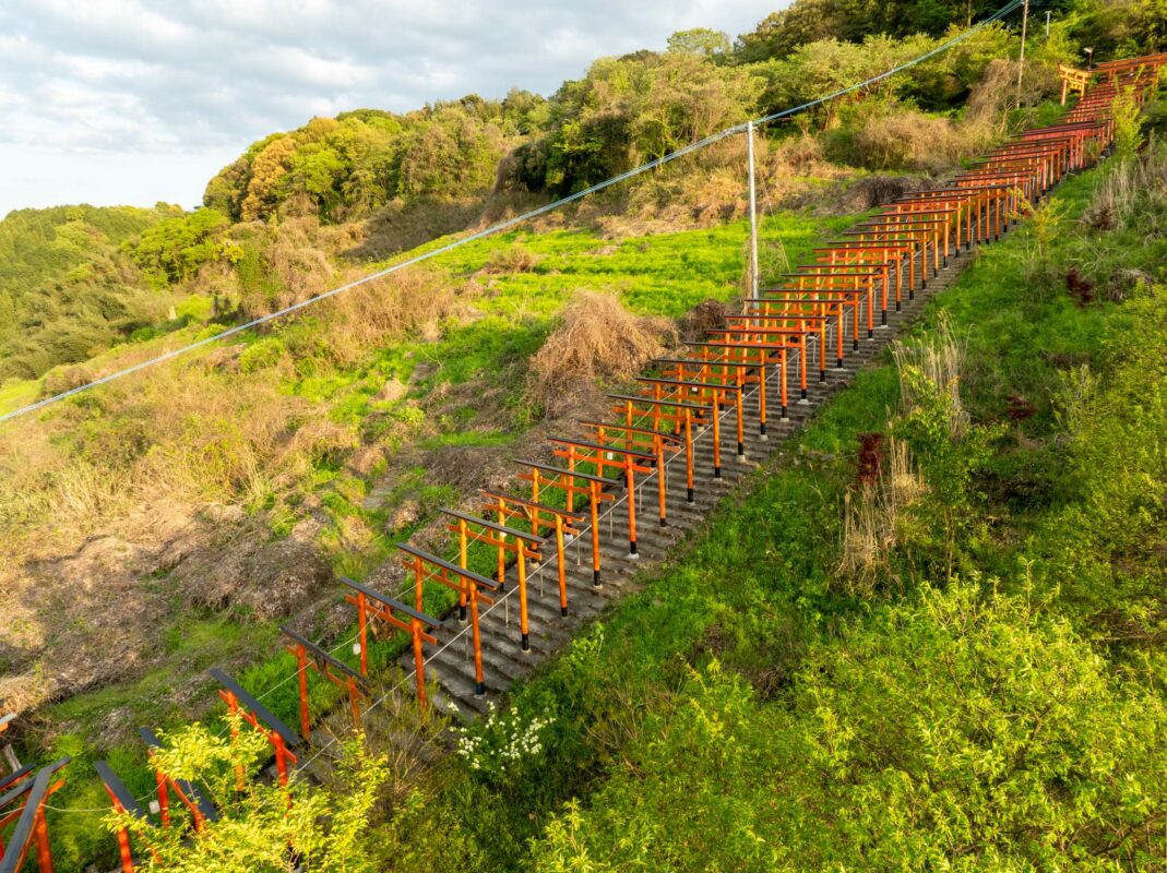 Vermilion torii gate stairway climbing Ukiha Inari Shrine hillside in lush greenery.