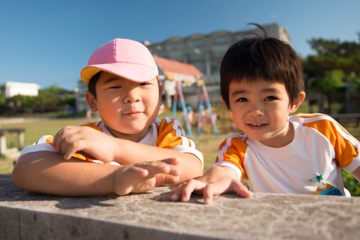 Two smiling children leaning on a stone ledge at a sunny Miyako Island park.