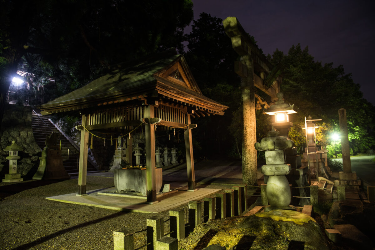 Heisenji Hakusan Shrine at night, lantern-lit wooden hall with mossy stone lanterns and forest path