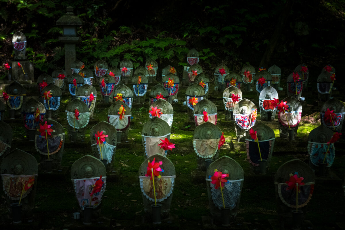 Moss garden Jizo statues with colorful bibs and pinwheels at Kongōrin-ji Temple, Japan.