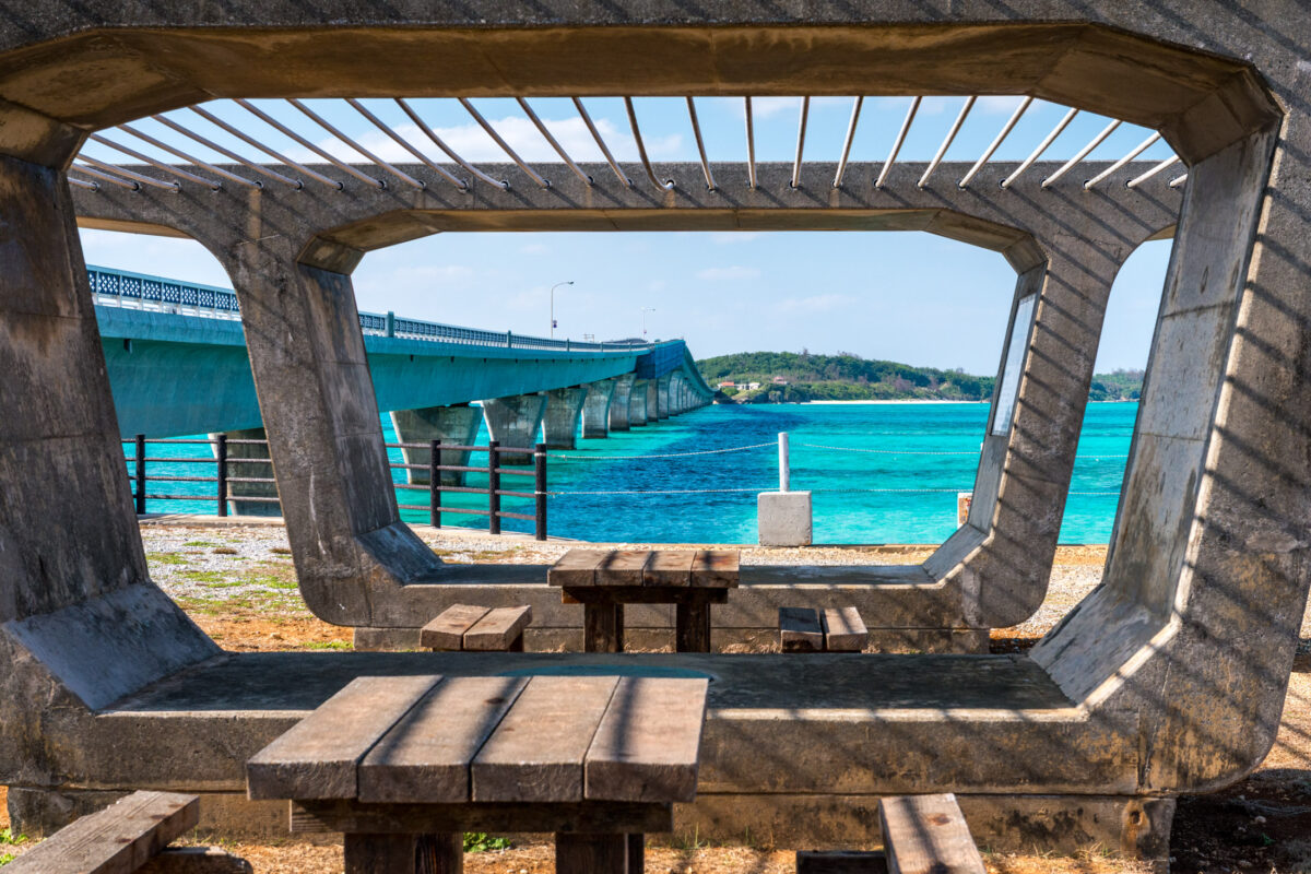 Concrete shelter framing Miyako Island turquoise ocean and bridge view under clear blue sky.