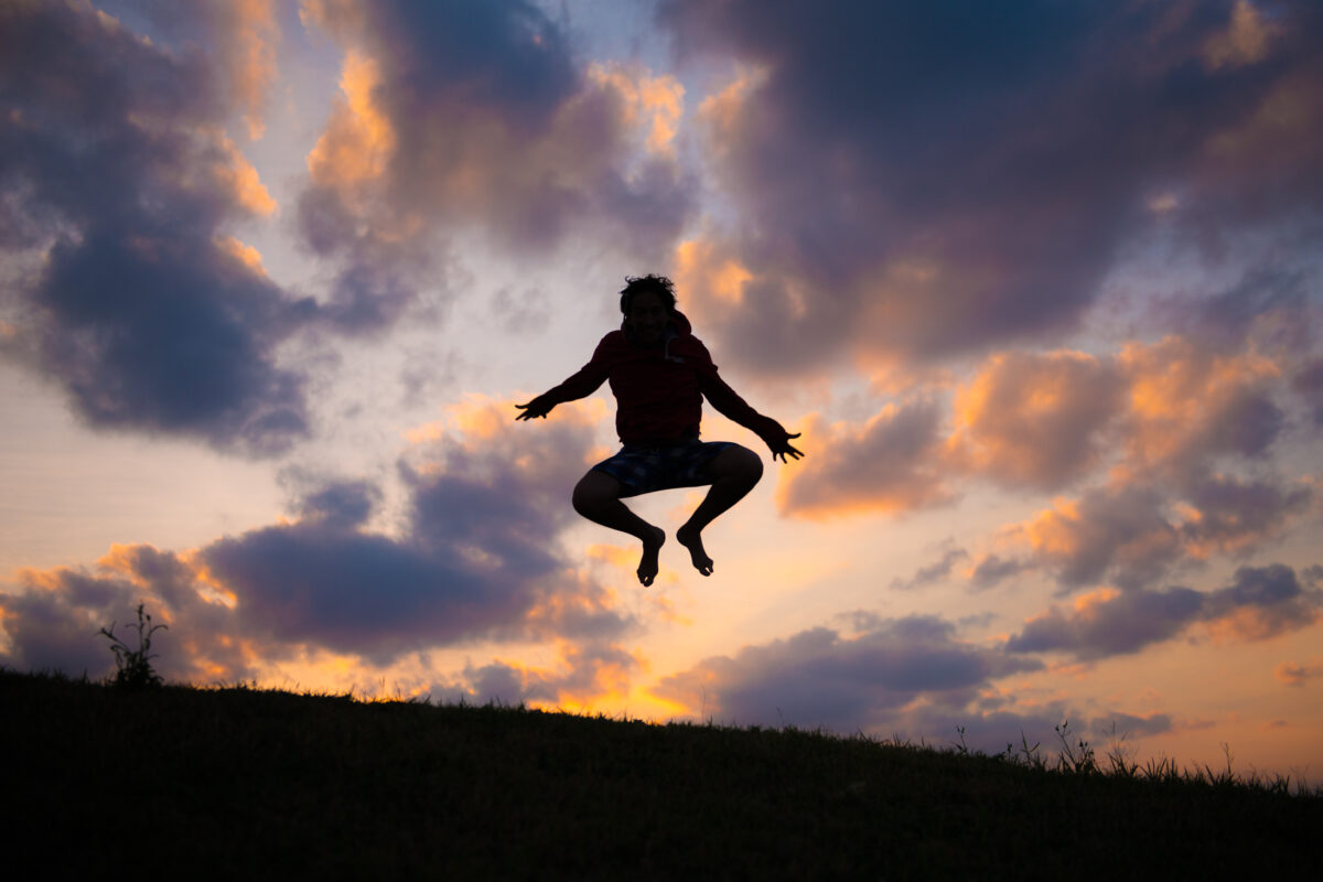 Silhouette jumping over grassy ridge at Miyako Island sunset with dramatic clouds