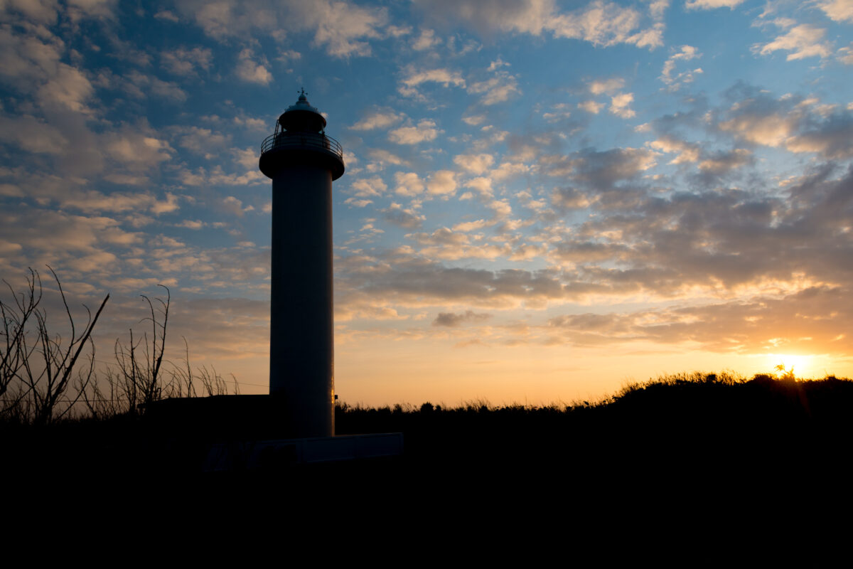 Silhouetted lighthouse on Miyako Island at sunset under golden clouds