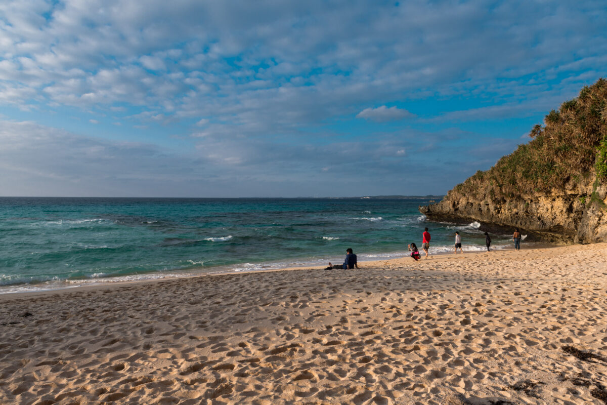 Turquoise beach and rocky cove on Miyako Island, Japan under partly cloudy sky.