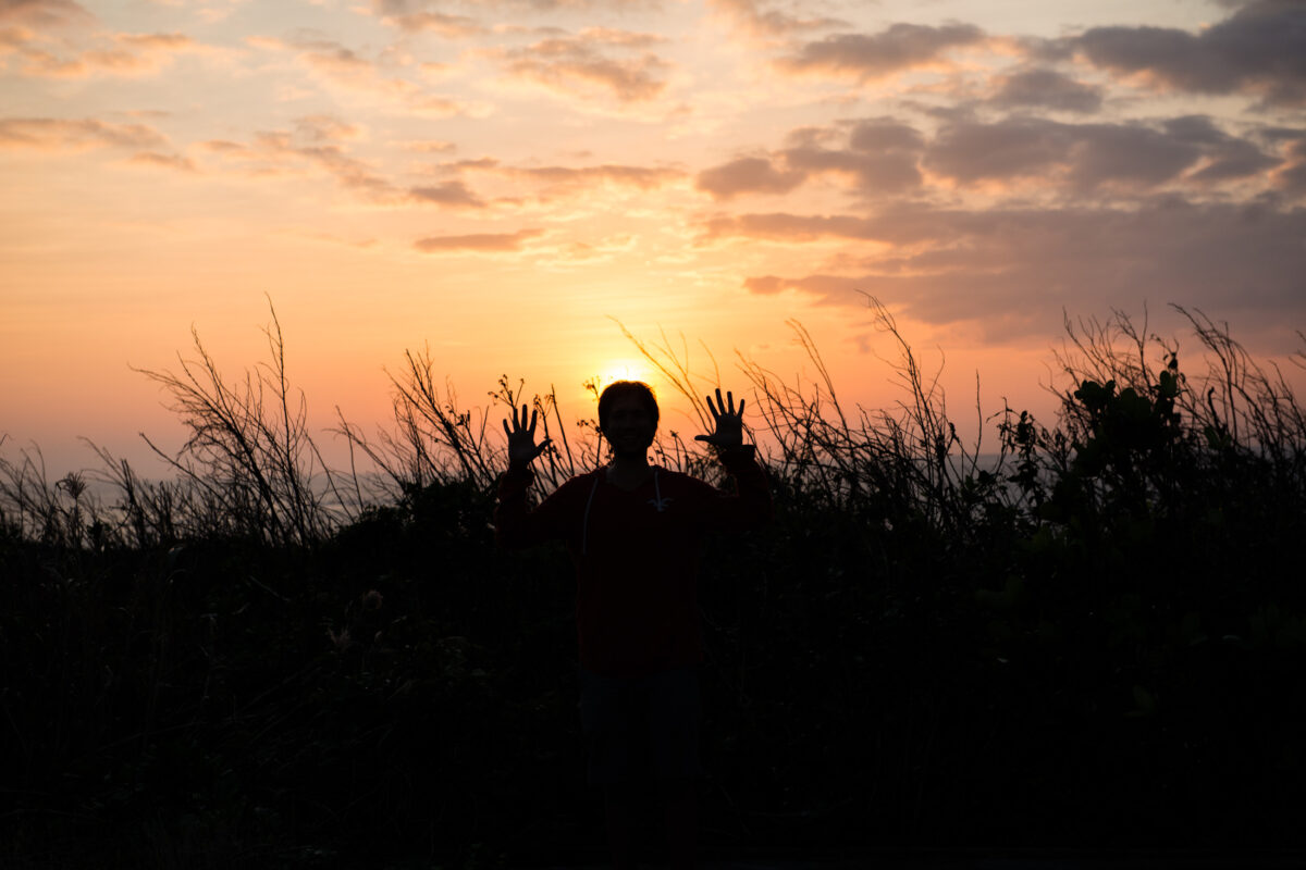 Person silhouette in coastal grasses at Miyako Island sunset with golden clouds