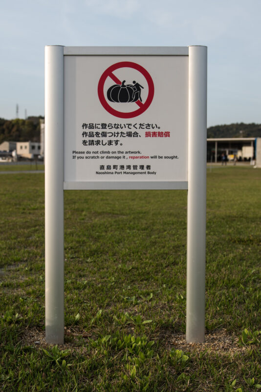 Naoshima art site no photography sign with red camera symbol in grassy field.