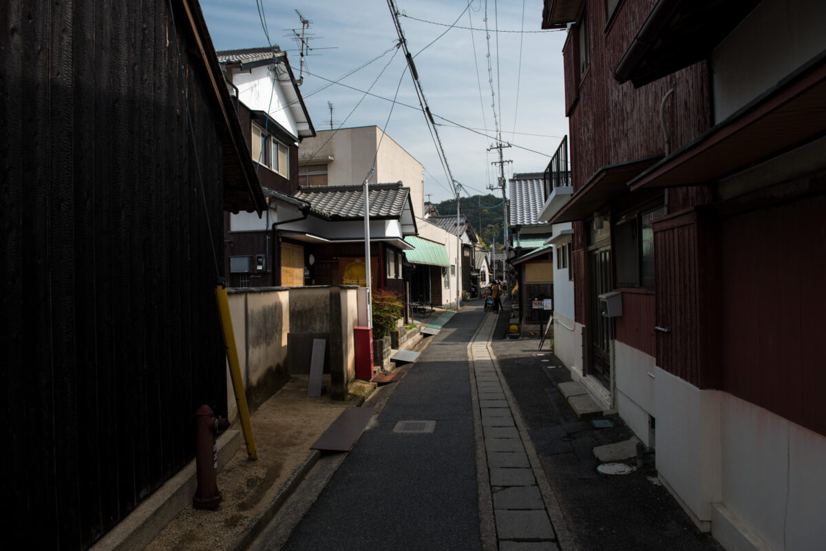 Quiet Naoshima, Japan residential alley with wooden houses, power lines, and distant hills.