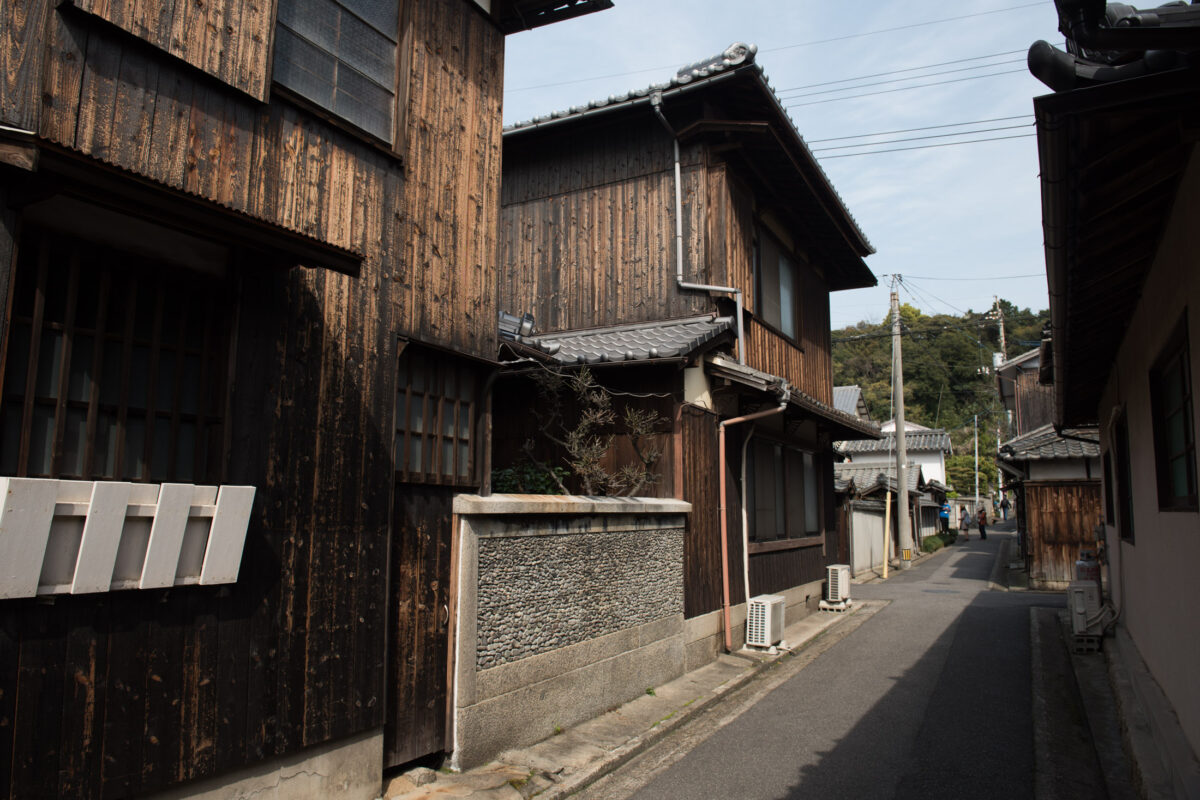Quiet street in Naoshima, Japan, lined with weathered wooden houses and tiled roofs.