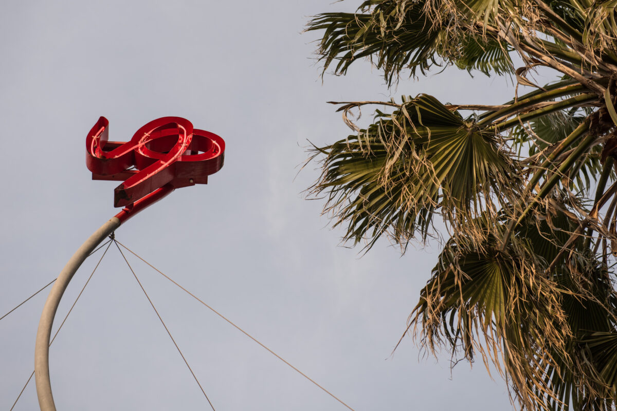 Red abstract ribbon sculpture on tall pole against cloudy sky, Naoshima Island