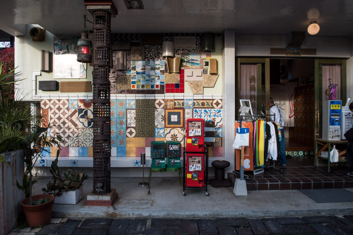 Tile mosaic storefront on Naoshima Island with red vending machine and clothing rack.