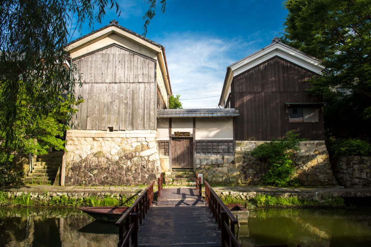 Wooden bridge over Omihachiman canal leading to historic Japanese storehouses on stone foundations