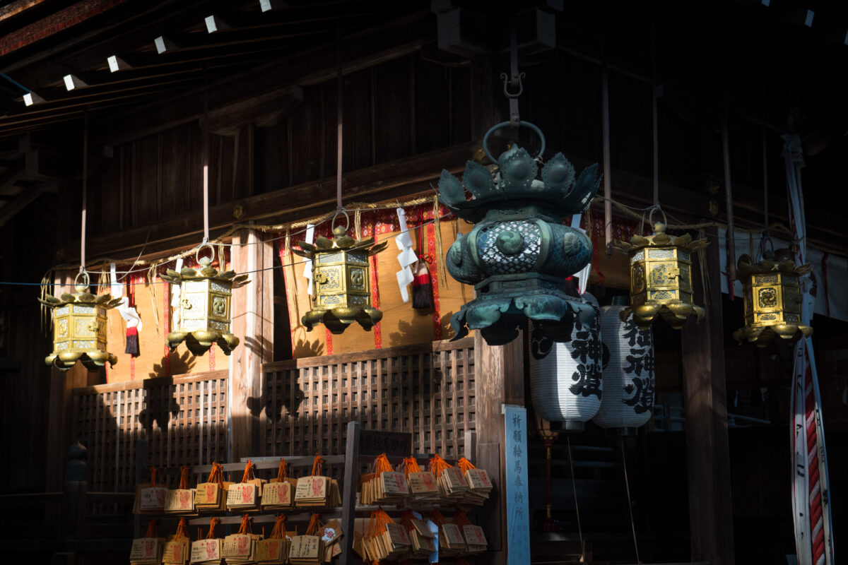 Ornate hanging lanterns in a dim Omihachiman Japanese shrine interior with votive plaques