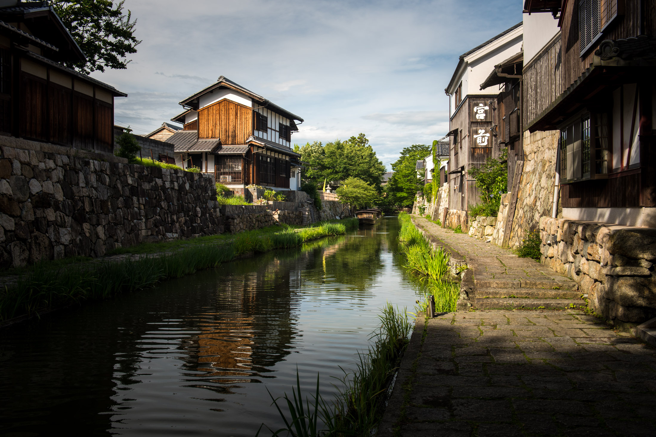 Omihachiman canal in Japan lined with traditional wooden townhouses and a stone walkway.