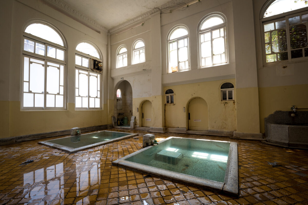 Historic Sekizenkan Ryokan onsen bathhouse interior with twin hot spring pools and arched windows.