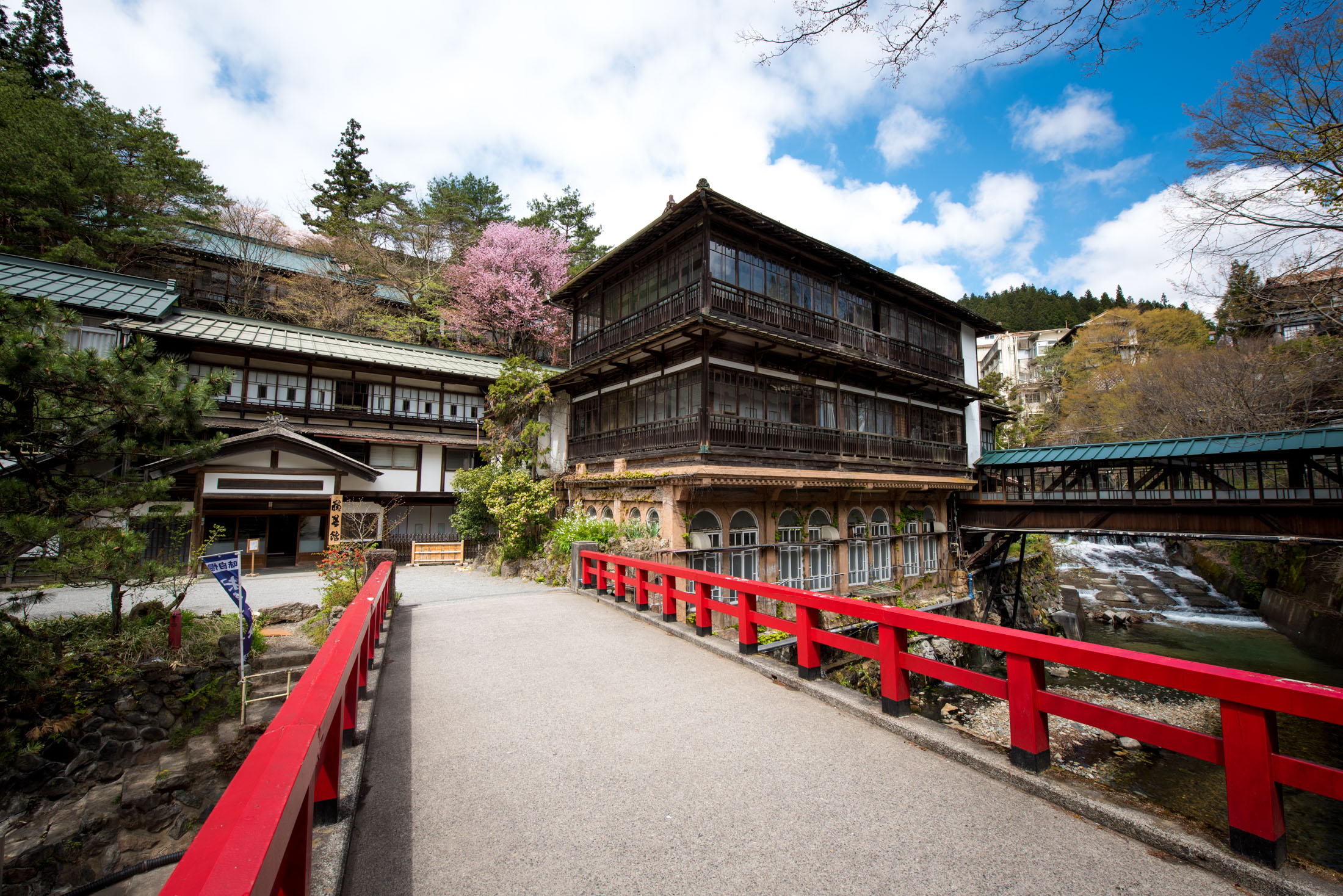 Sekizenkan Ryokan wooden inn beyond red bridge, spring cherry blossoms, Japan