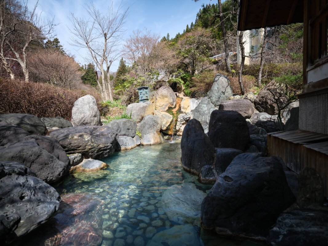 Steaming rock-lined outdoor hot spring at Shima Onsen, Japan, surrounded by forest.