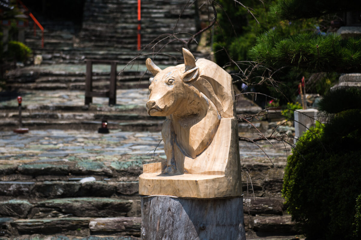 Carved wooden ox statue by stone steps at Wakaura Tenmangu Shrine, Wakayama Japan.