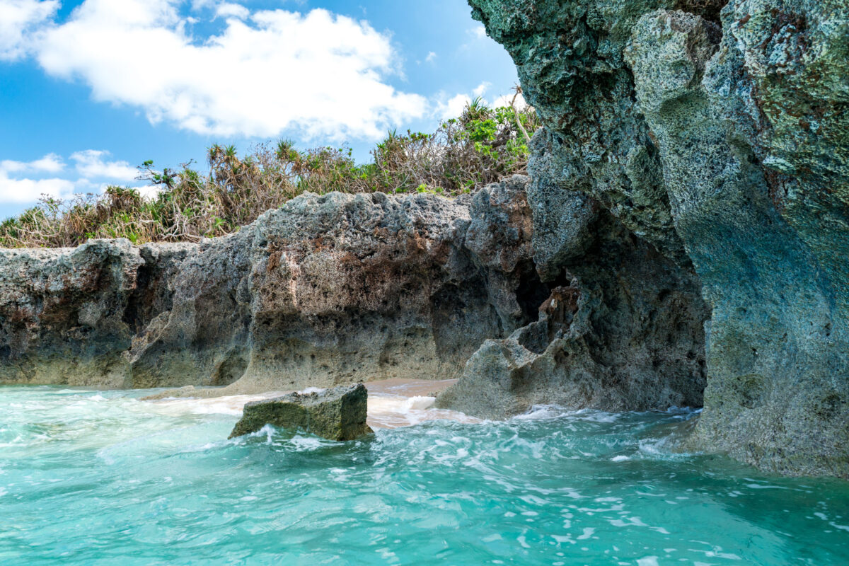 Turquoise cove and rugged limestone cliffs on Miyako Island under a bright blue sky.
