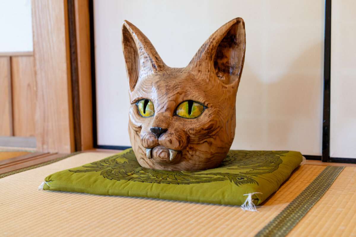Wooden cat guardian head on green cushion atop tatami in Japanese temple room