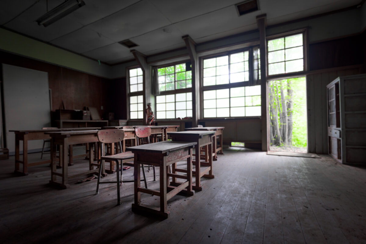 Abandoned school classroom with dusty desks, sunlight through windows, vines creeping inside