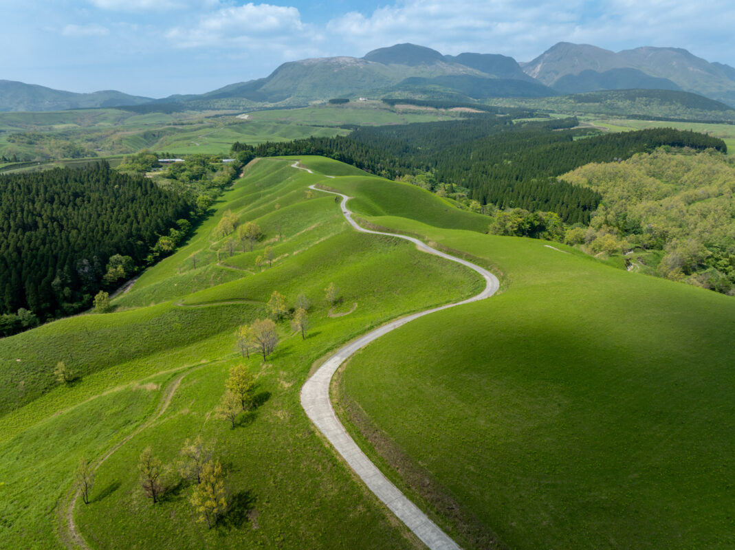 Winding path along Ogi terrace fields, rolling green hills, forests, and distant mountain range.