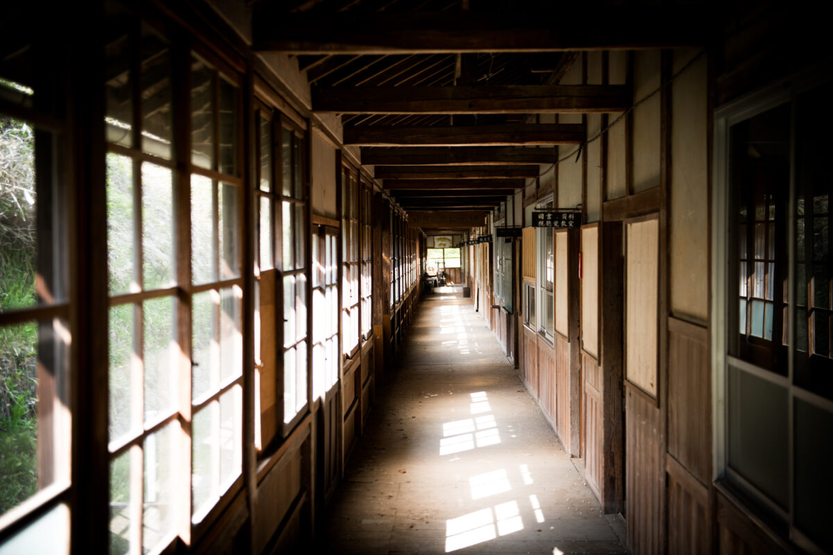 Sunlit wooden corridor at Sakamoto School with windows, sliding classroom doors, and nostalgic atmosphere.